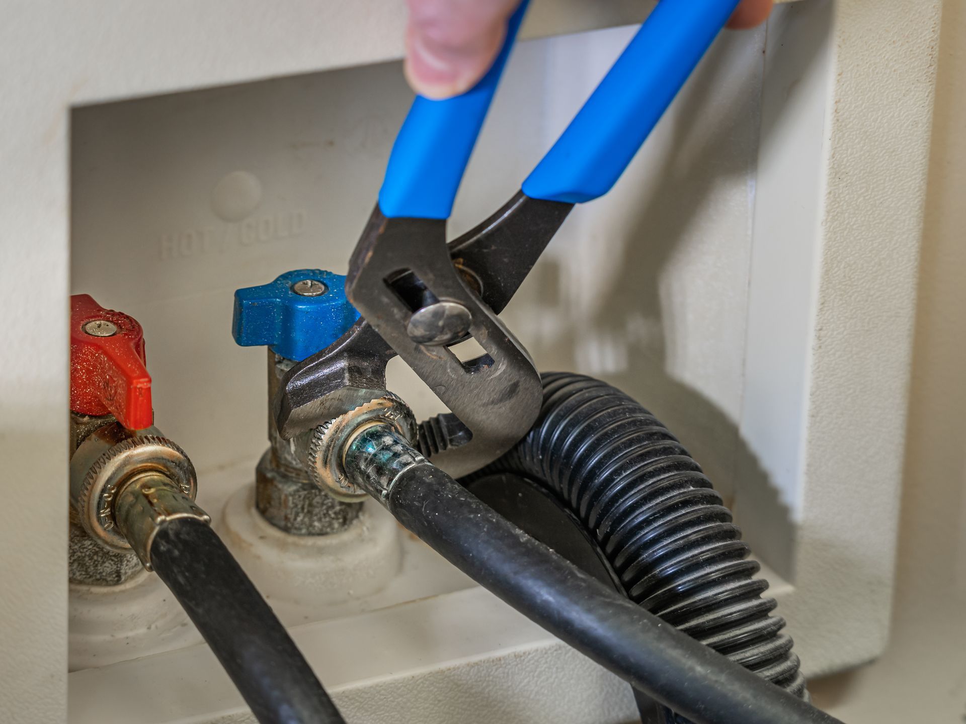 Hand using pliers to tighten a blue shutoff valve on a plumbing manifold with hoses attached