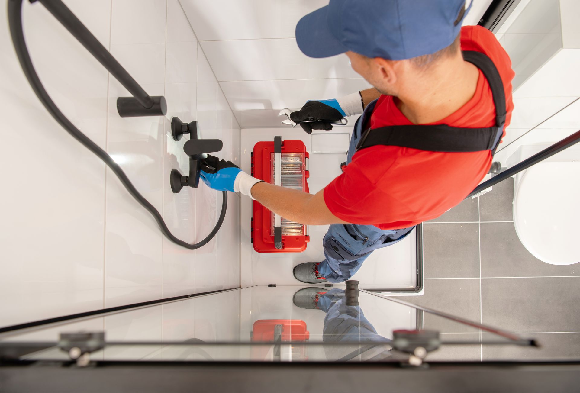 Worker in orange safety vest using a fire extinguisher on a wall-mounted unit in a white stairwell