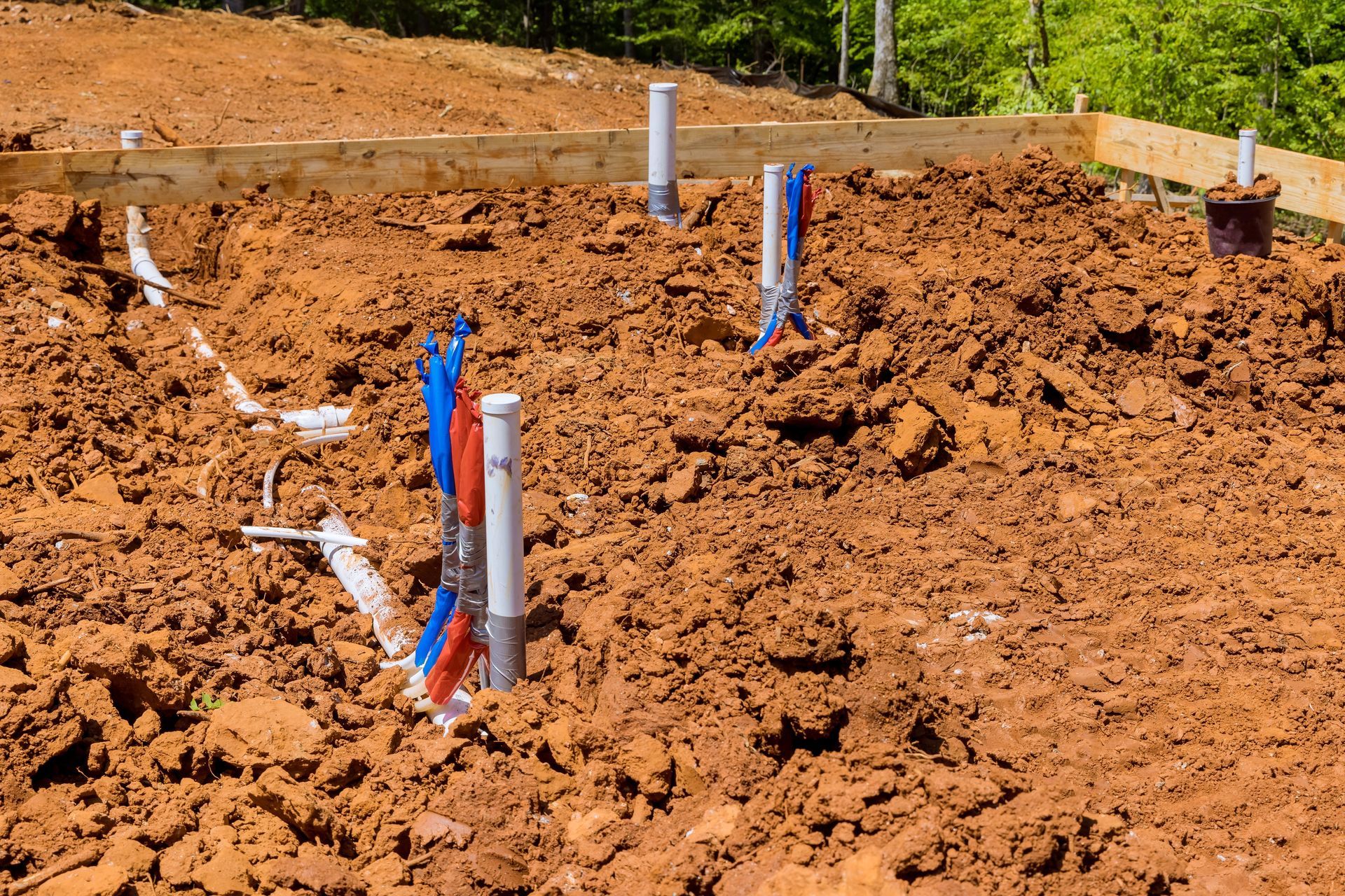Utility pipes protruding from freshly dug red soil at a construction site