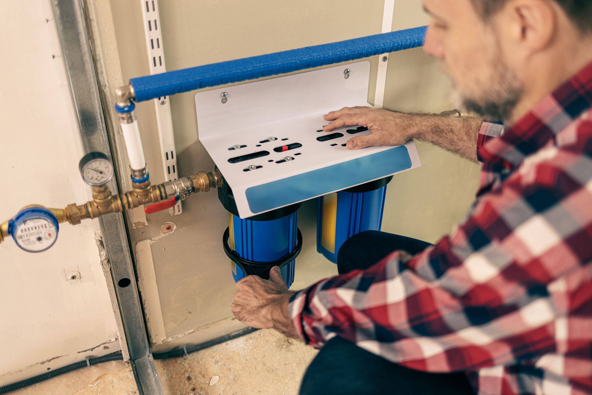 Technician adjusting a blue water filtration unit with pressure gauge and pipes indoors