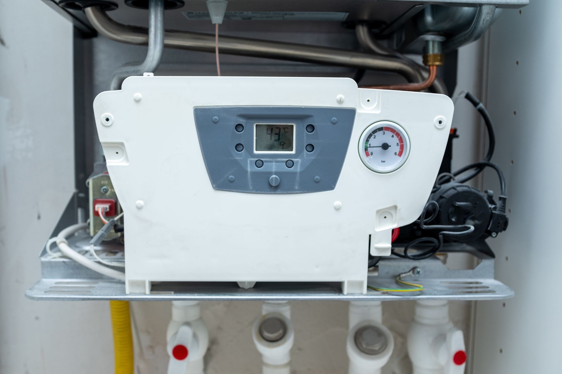 White wall-mounted appliance with digital display and gauge inside a cabinet, with pipes below.