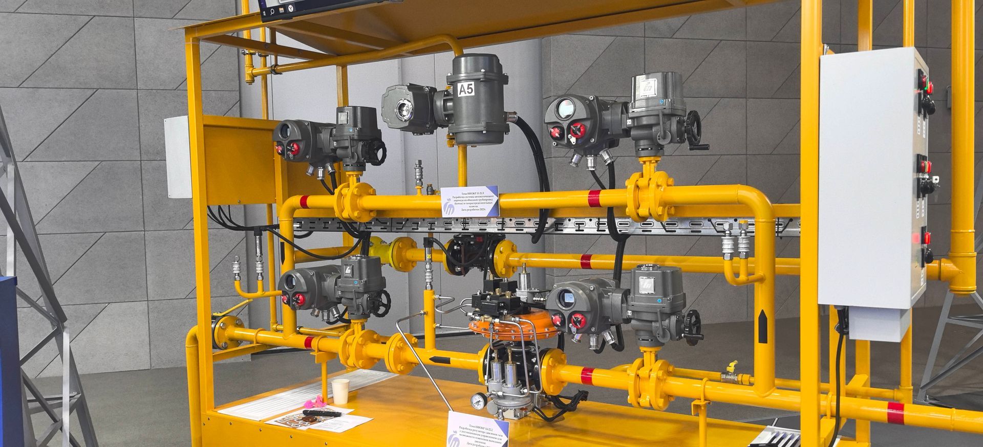 Yellow industrial gas piping and valves mounted on a frame with a control box in a utility room