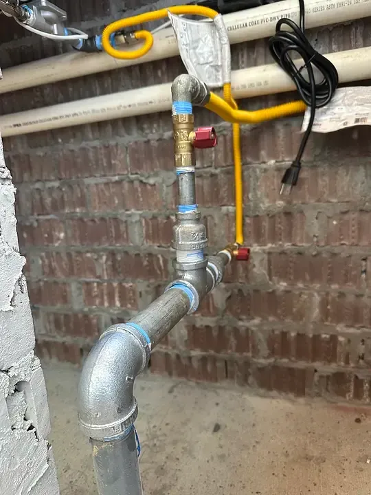 Yellow gas pipe and metal plumbing fittings against a brick wall, with a valve and hanging cable.