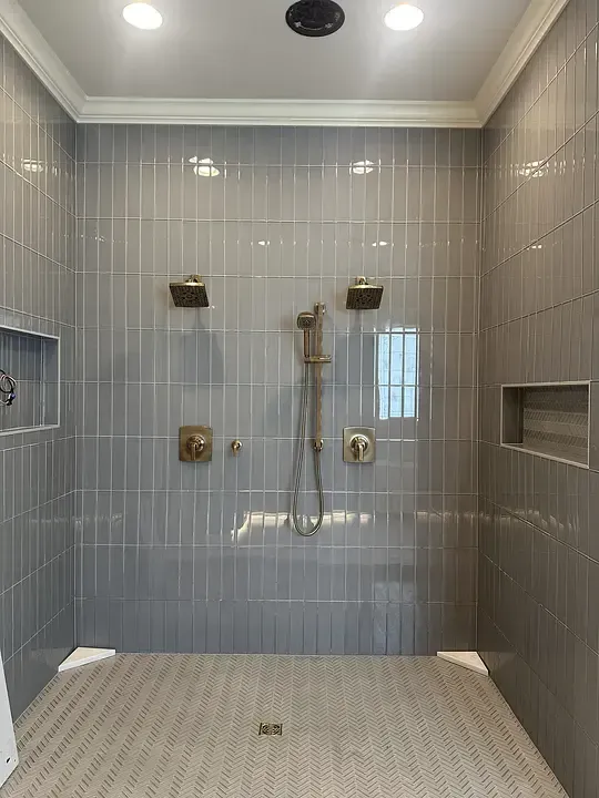 Modern tiled bathroom shower with brass fixtures, glass shelf, and bench niche
