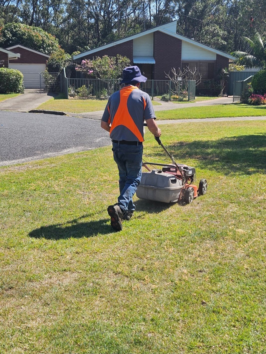 Person in Orange Vest Mowing a Lawn in A Suburban Yard — Coast 2 Coast Disability Support Services in Taree, NSW