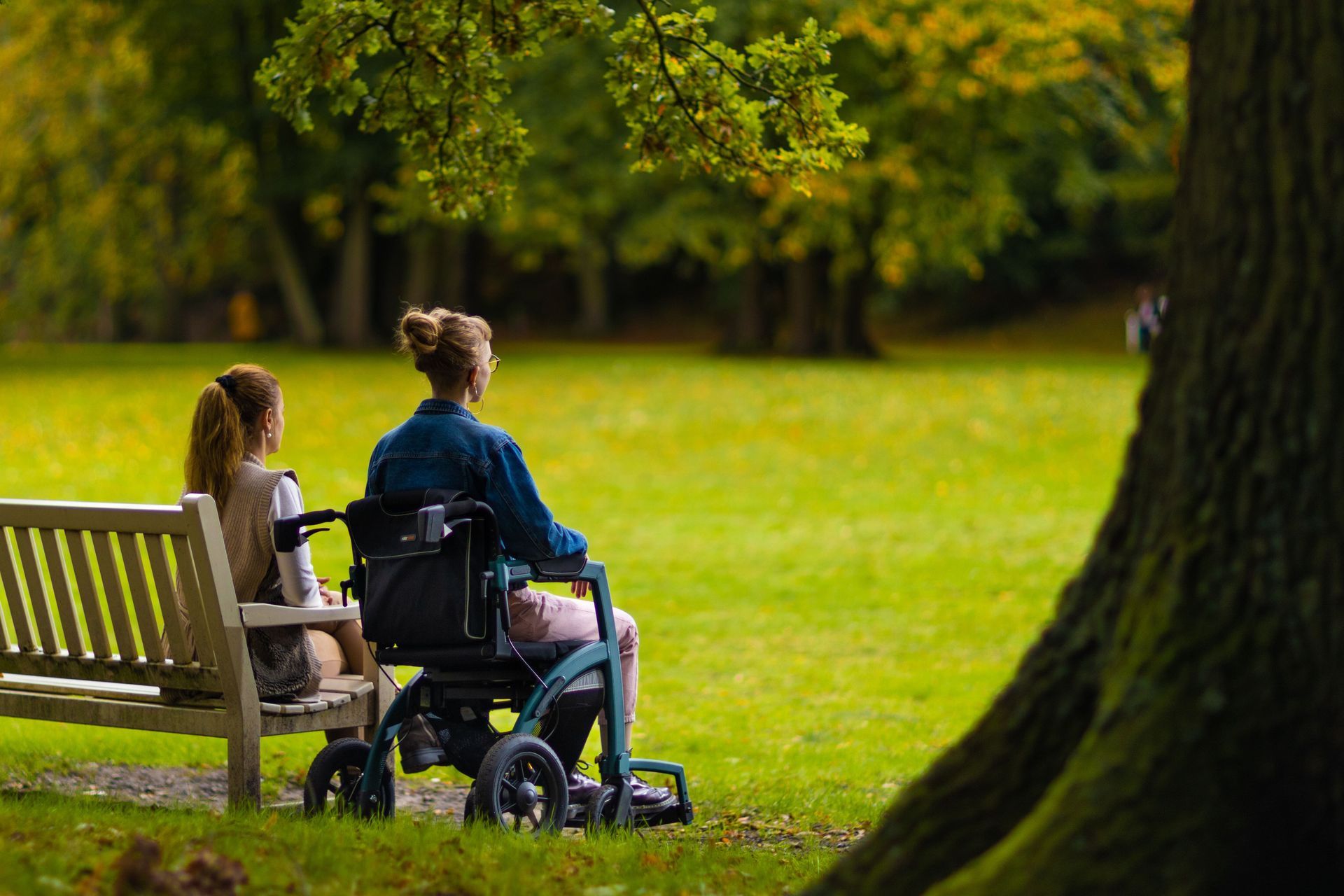 Man Pushing a Woman in A Wheelchair Along a Sunny Path — Coast 2 Coast Disability Support Services in Taree, NSW