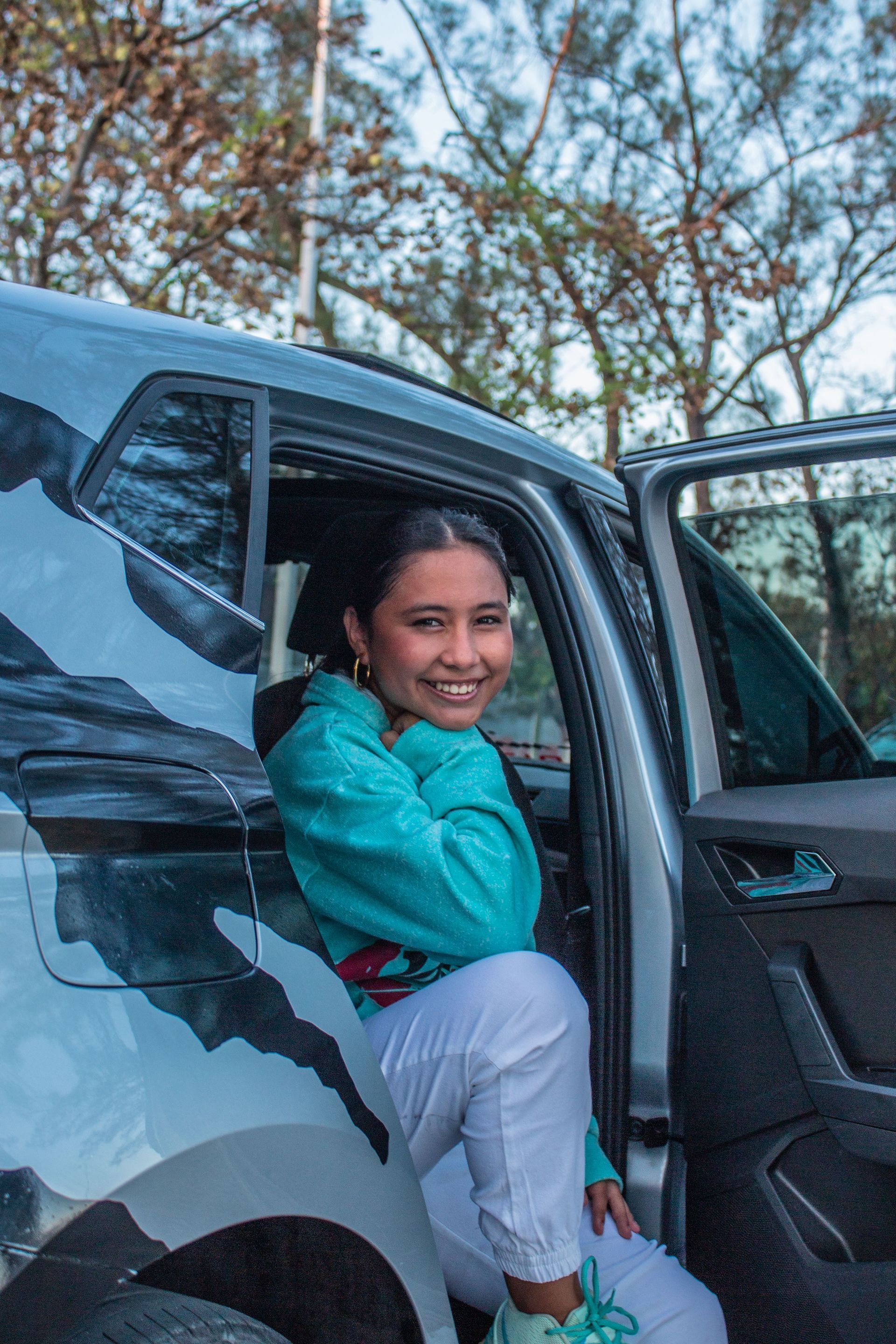 Smiling Woman in A Teal Jacket Stepping out Of a Gray Car — Coast 2 Coast Disability Support Services in Taree, NSW