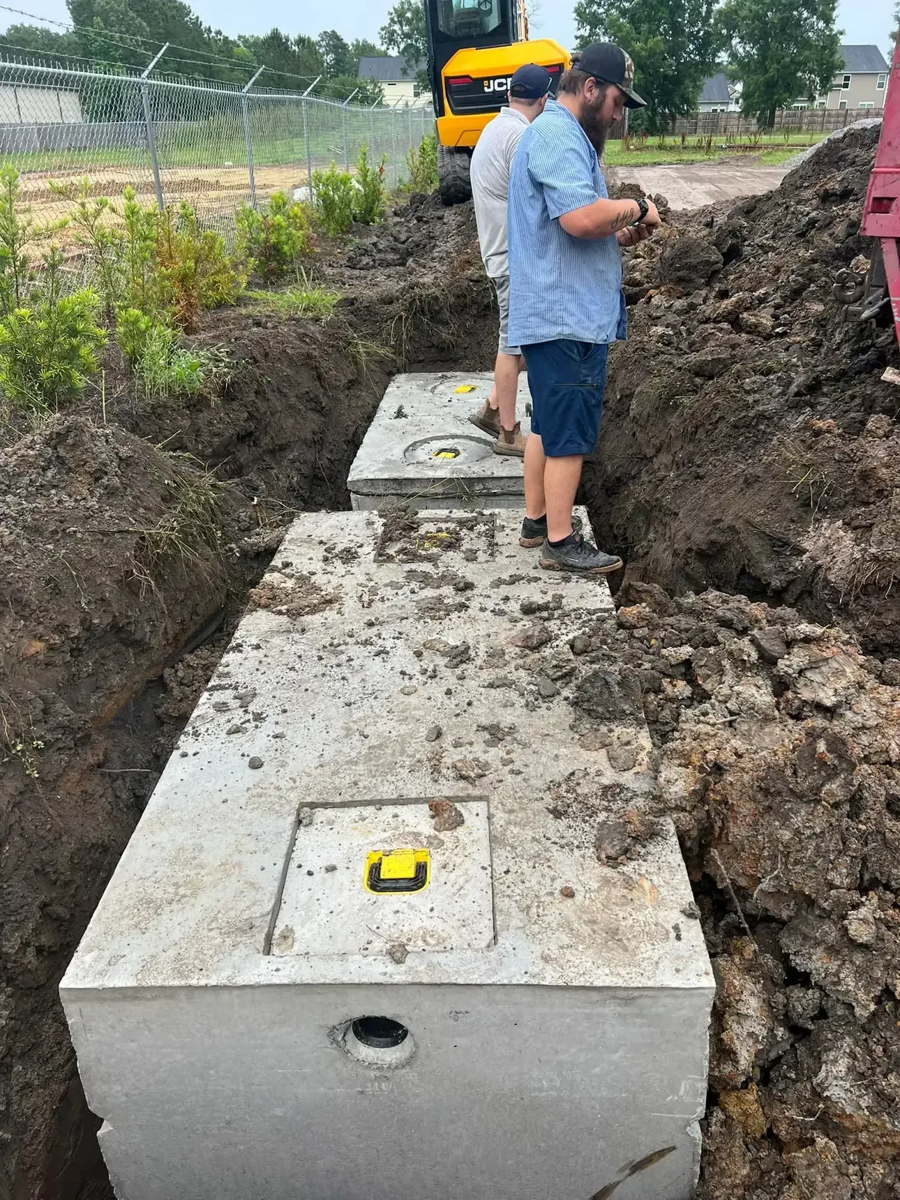 A man is standing in the dirt next to a septic tank.