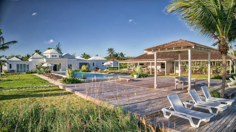 Tropical resort patio with lounge chairs, pergola, palm trees, and white villas by the water