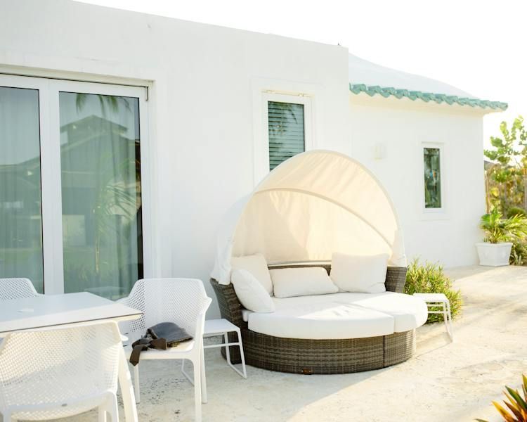 White patio with wicker daybed, round table, and chairs beside a modern house exterior