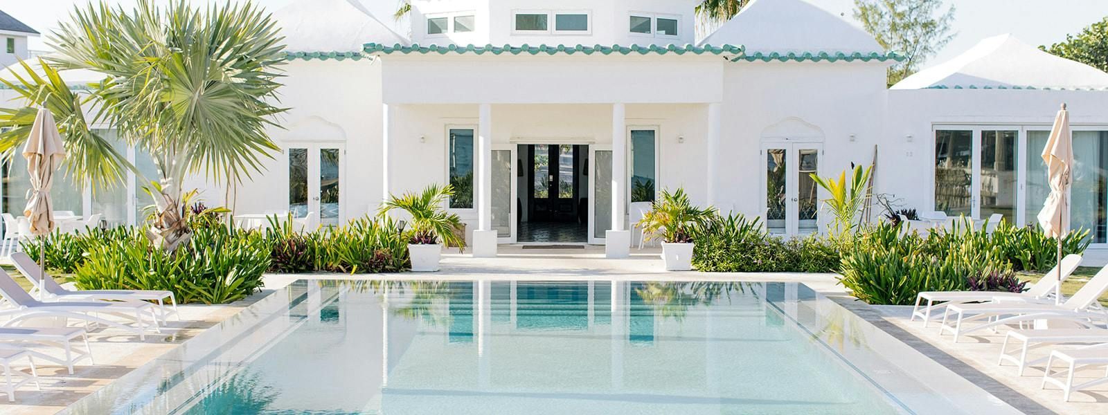 Bright white luxury villa with a central pool, palm trees, and lounge chairs in a sunny courtyard