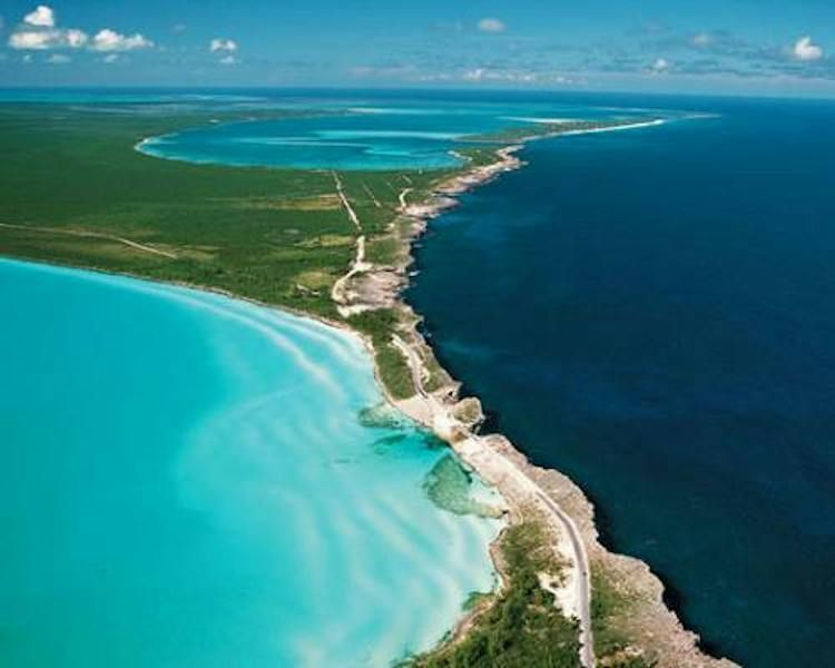 Aerial view of a narrow tropical island separating bright turquoise water from deep blue ocean.