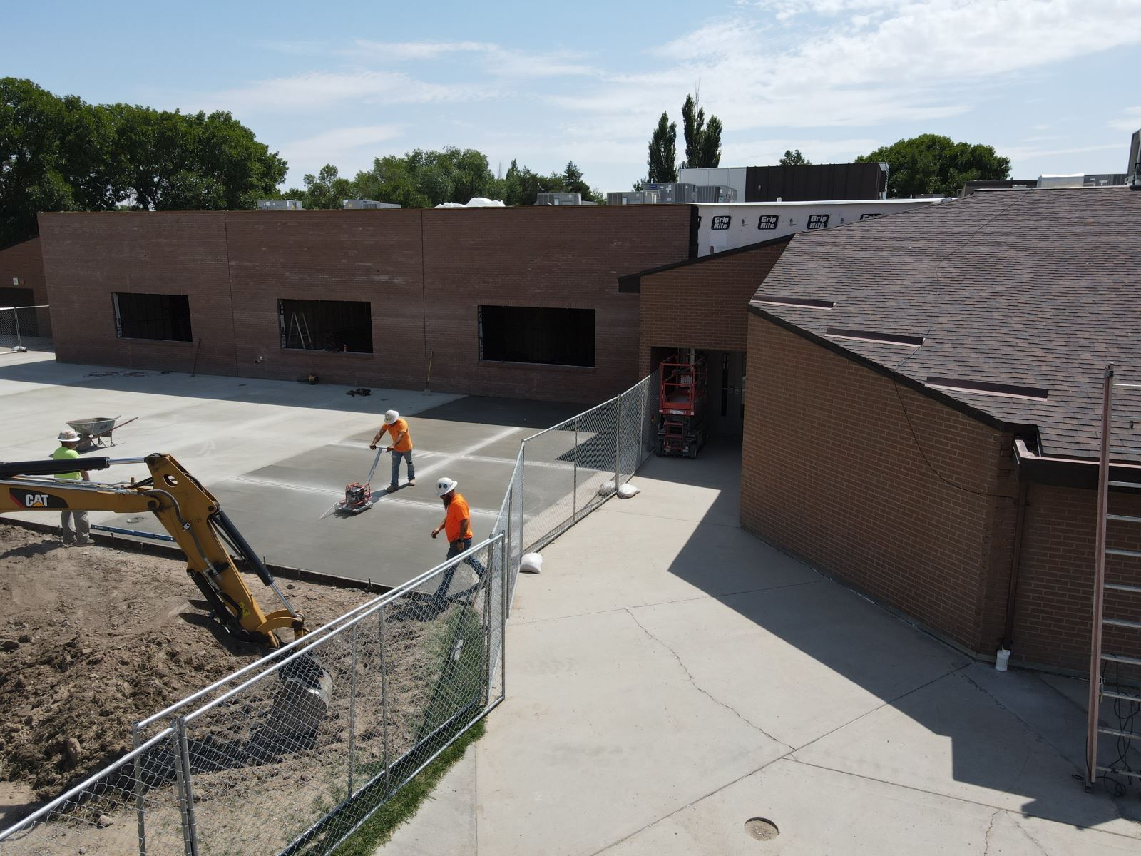 Construction workers are working on a concrete driveway in front of a brick building