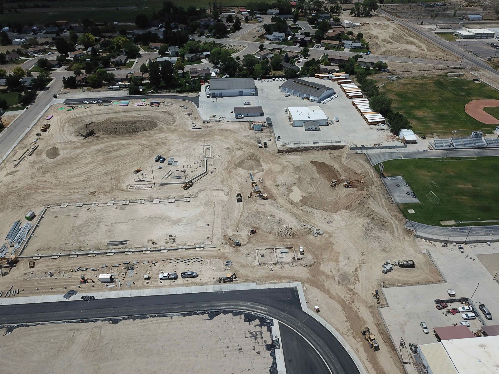 An aerial view of a construction site with a baseball field in the background