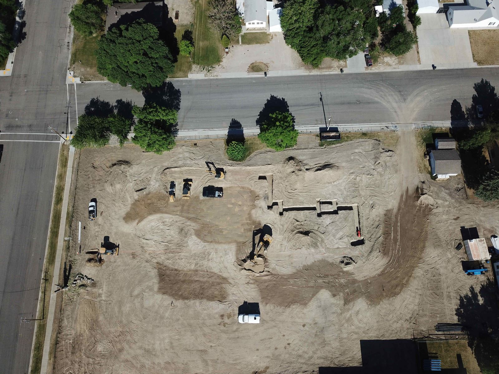 An aerial view of a dirt field with trees and houses in the background