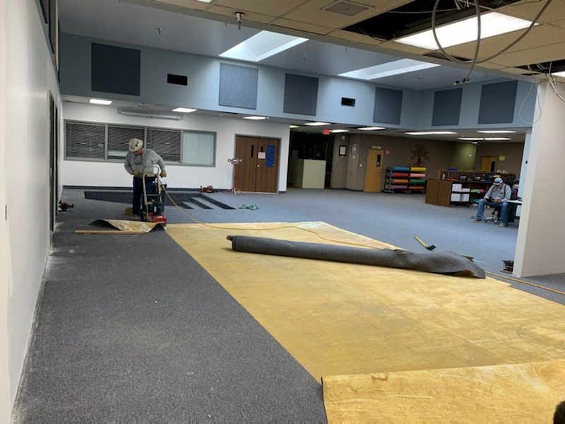 A man is moving a roll of carpet in a large room.