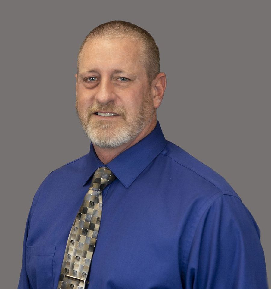 A man in a blue shirt and tie is smiling for the camera.