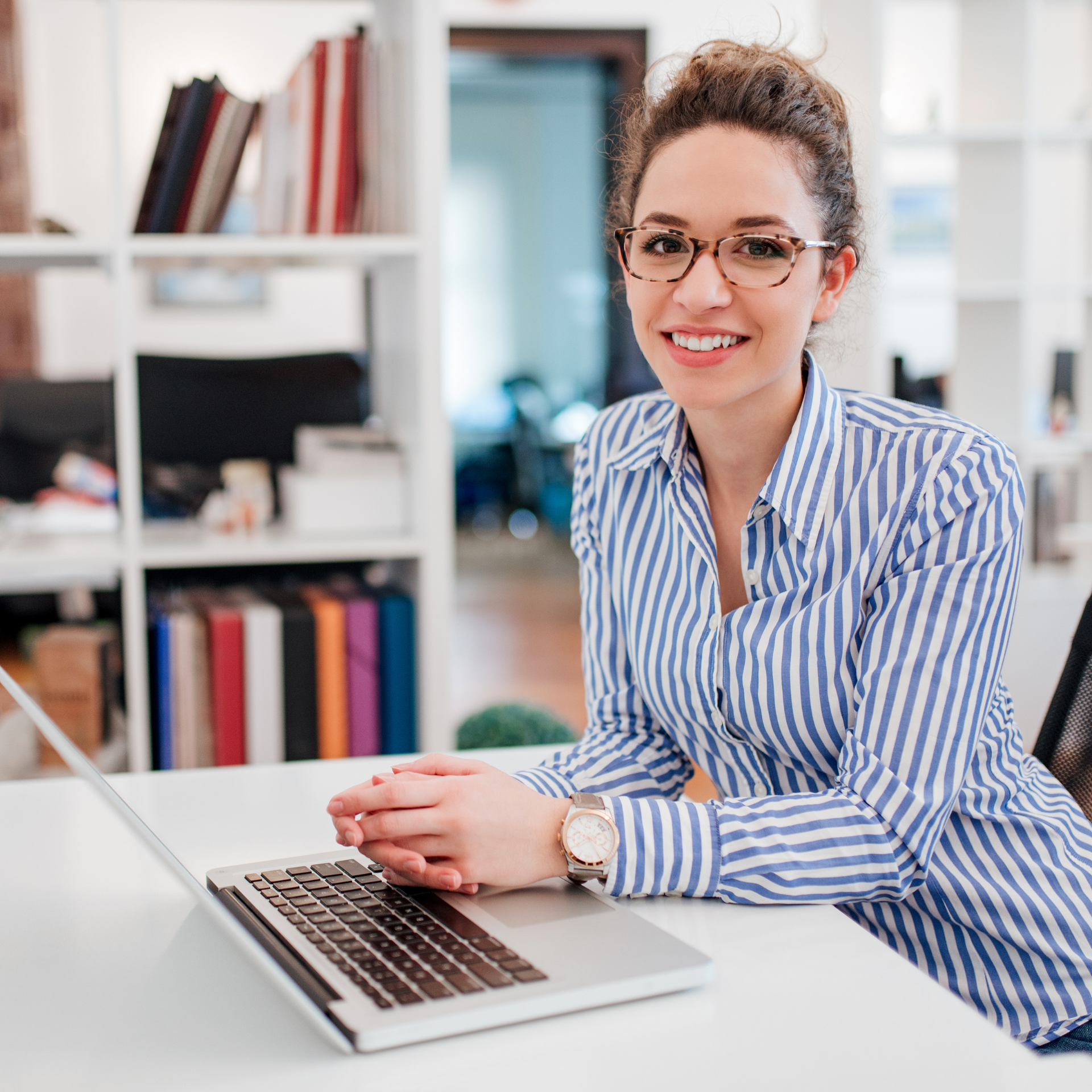 A woman wearing glasses is sitting at a desk with a laptop computer.