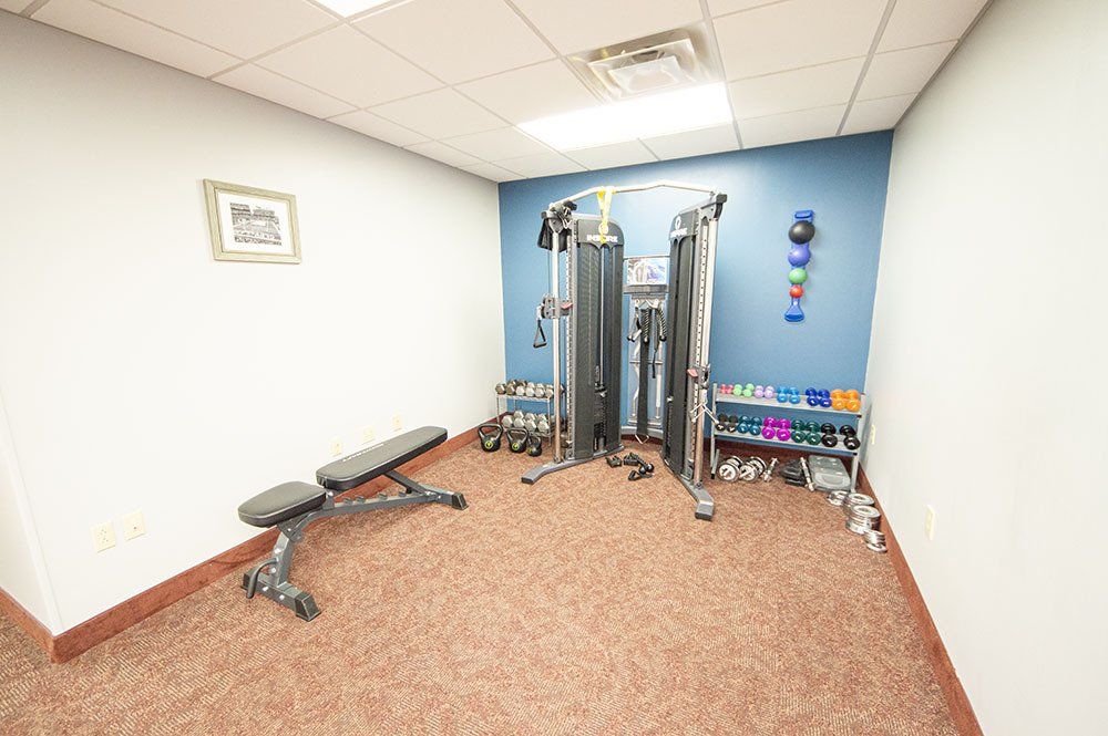 Small home gym with weights, bench, and cable machine; blue accent wall and brown carpet.