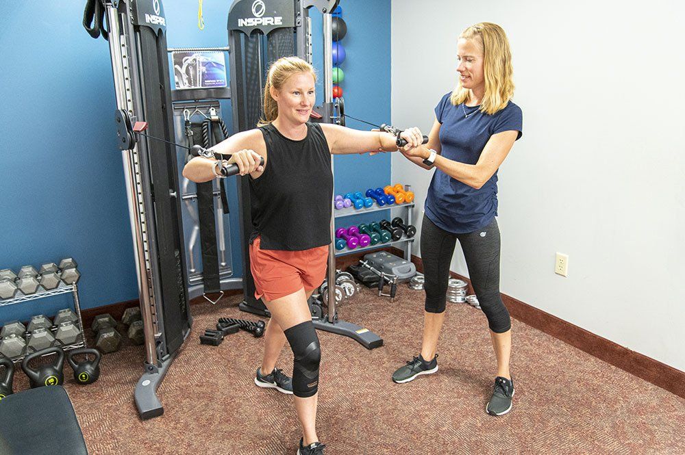 Woman exercising with a trainer at a gym. Woman is using a cable machine. Trainer assists.