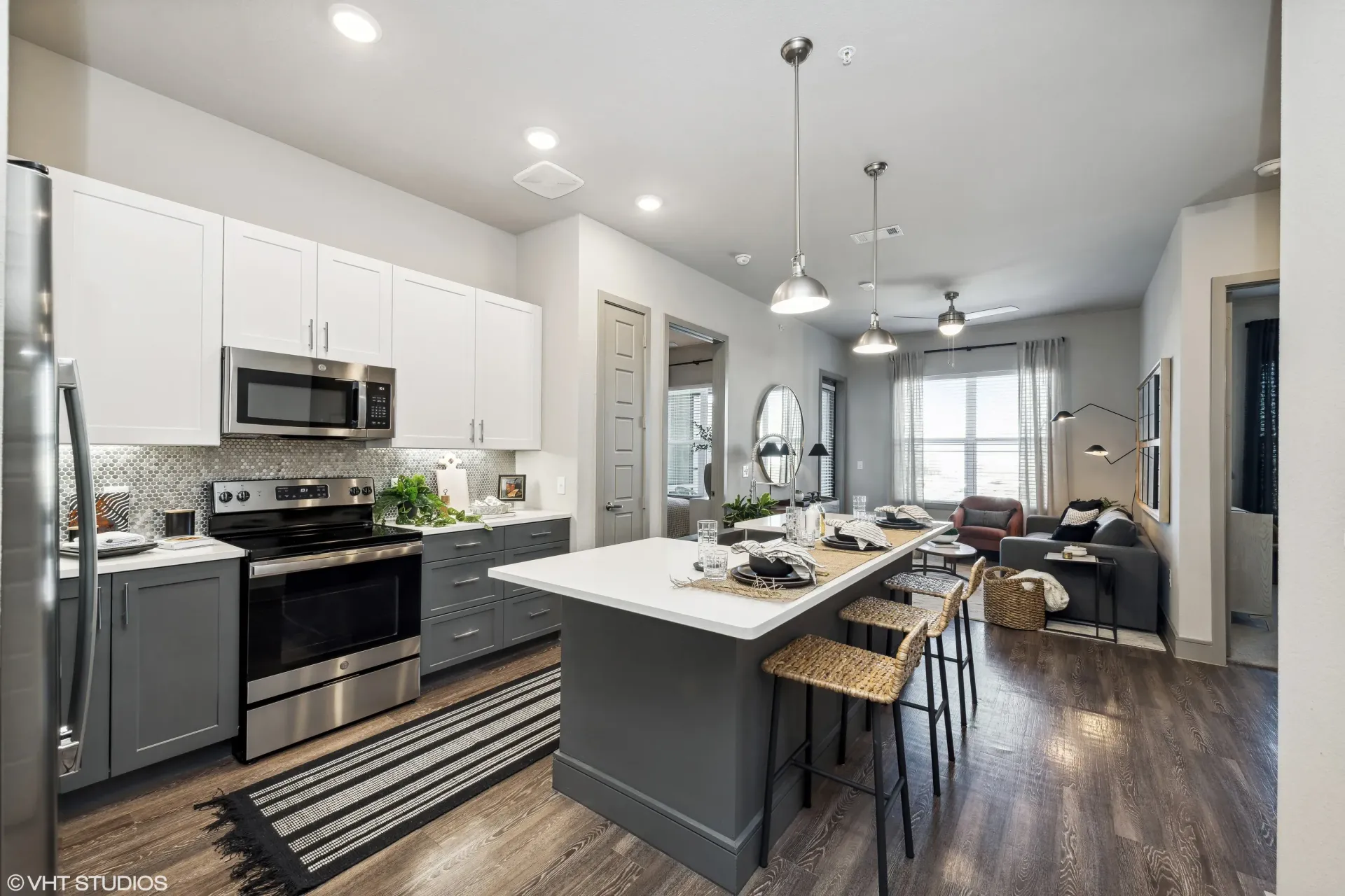 Open-concept kitchen with white upper cabinets, gray lower cabinets, stainless appliances, and island seating.