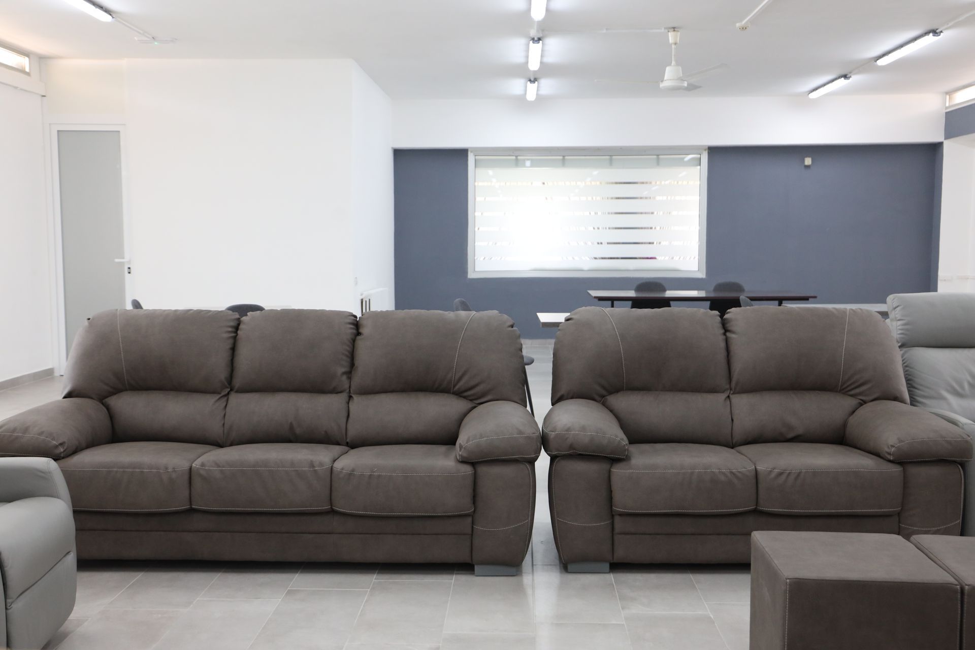 Due divani in tessuto grigio in uno showroom. Pareti e luci bianche. Piccolo pouf.