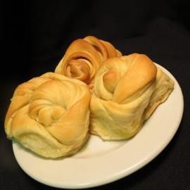 Three golden-brown bread rolls on a white plate against a dark background