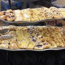 Trays of assorted pastries with icing and fruit toppings on a bakery display counter