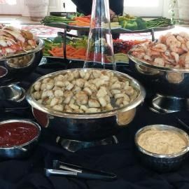 Buffet table with bowls of shrimp, dumplings, vegetables, and sauces on a black tablecloth.