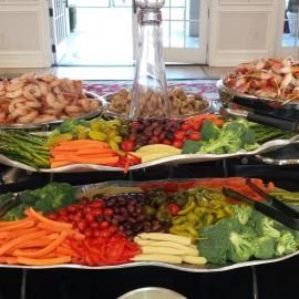 Buffet table with trays of colorful vegetables, shrimp, and fruit arranged for a meal