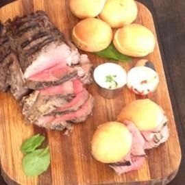 Sliced roast beef with rolls and garnished eggs on a wooden cutting board