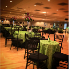 Empty banquet hall with round tables in green linens and black chairs under warm lighting