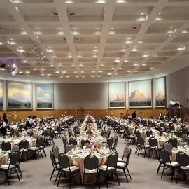 Banquet hall with round tables and chairs set for a formal dinner under a coffered ceiling