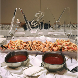 Seafood buffet with crab legs, red dipping sauces, and clear ice sculptures spelling “2014”