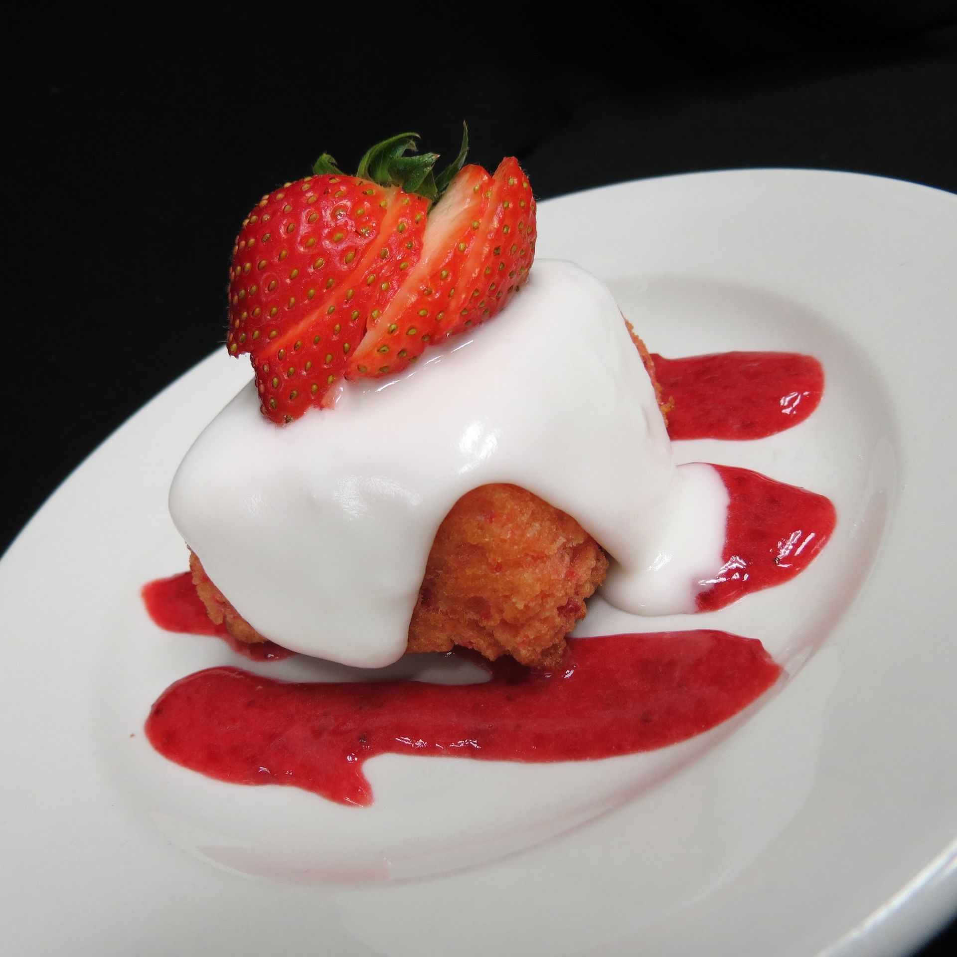 Strawberry dessert topped with white cream on a white plate with red sauce drizzle