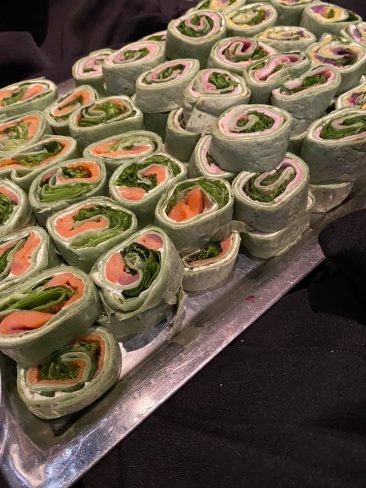 Tray of green wrap pinwheels with cream filling and red pepper, arranged in rows