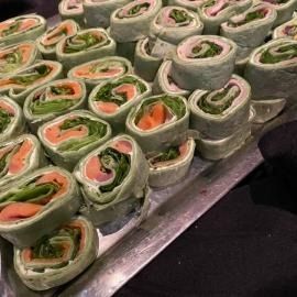 Tray of green wraps filled with salmon and greens, arranged in neat rows on a platter.