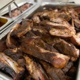 Tray of browned grilled meat pieces with a serving tongs at a buffet counter