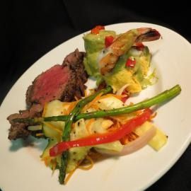 Plated steak with shrimp and colorful sautéed vegetables on a white dish