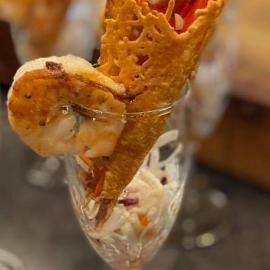 Shrimp cocktail in a clear glass, topped with a waffle cone garnish.