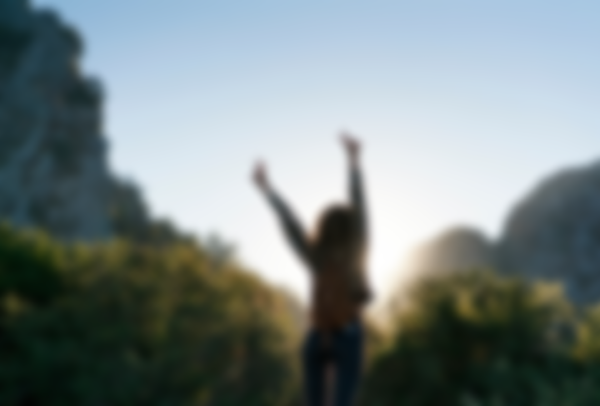 A woman is standing in front of a mountain with her arms in the air.