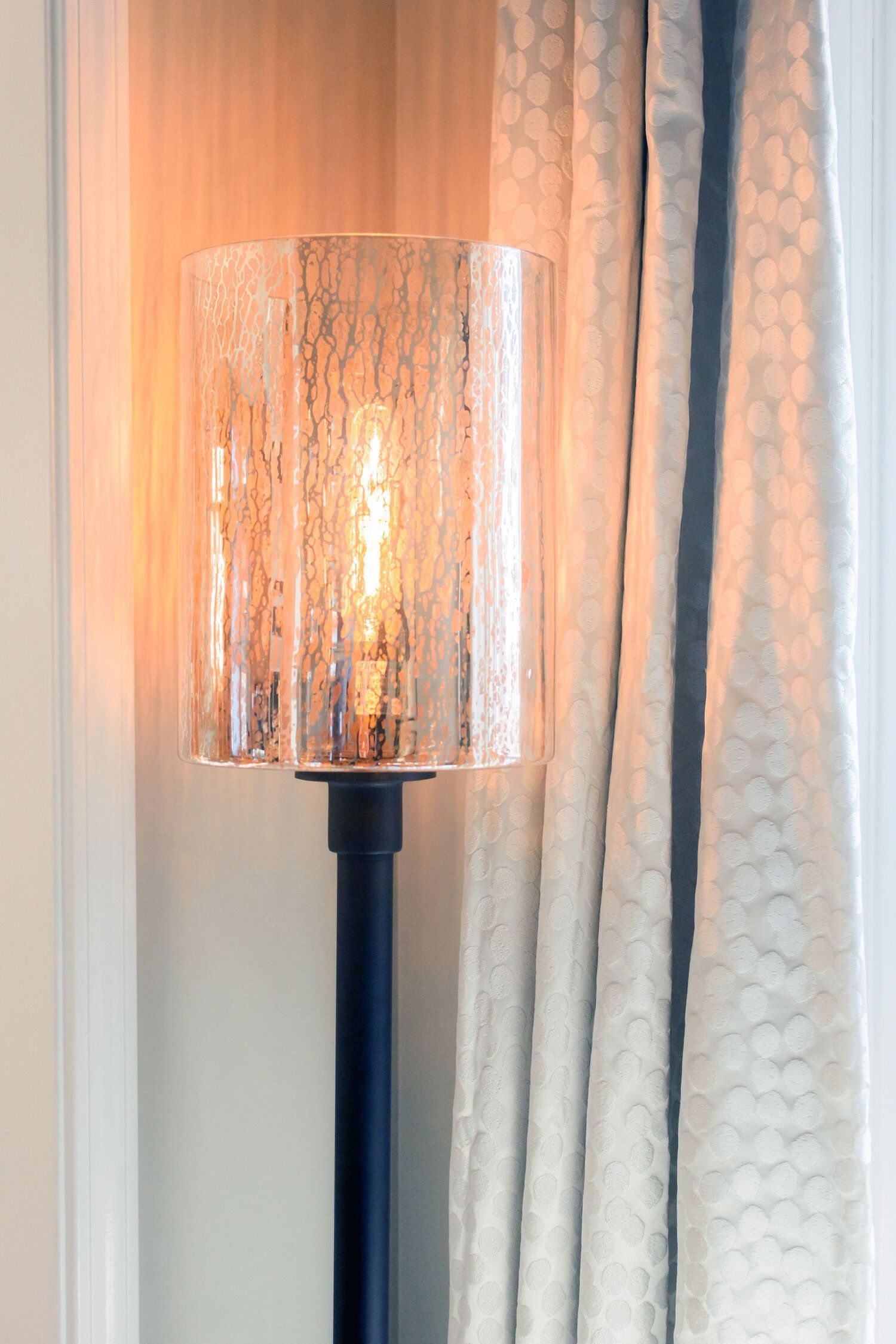 A lamp with a clear glass shade is sitting next to a window.