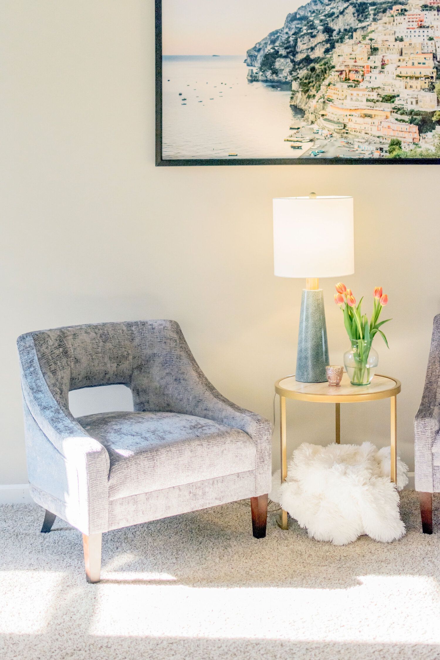 A living room with two chairs , a table , a lamp and a painting on the wall.