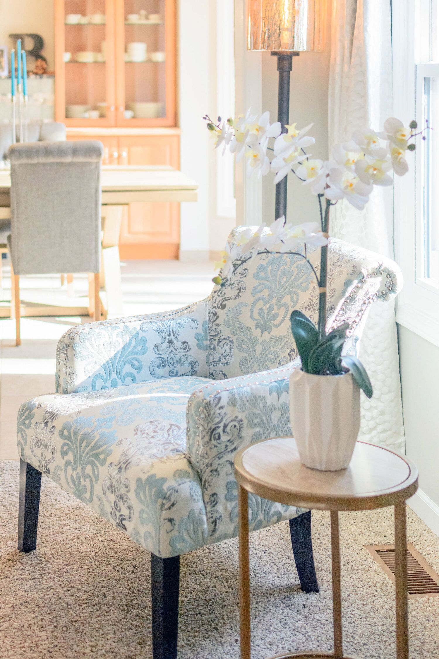 A chair is sitting next to a table with a vase of flowers on it.