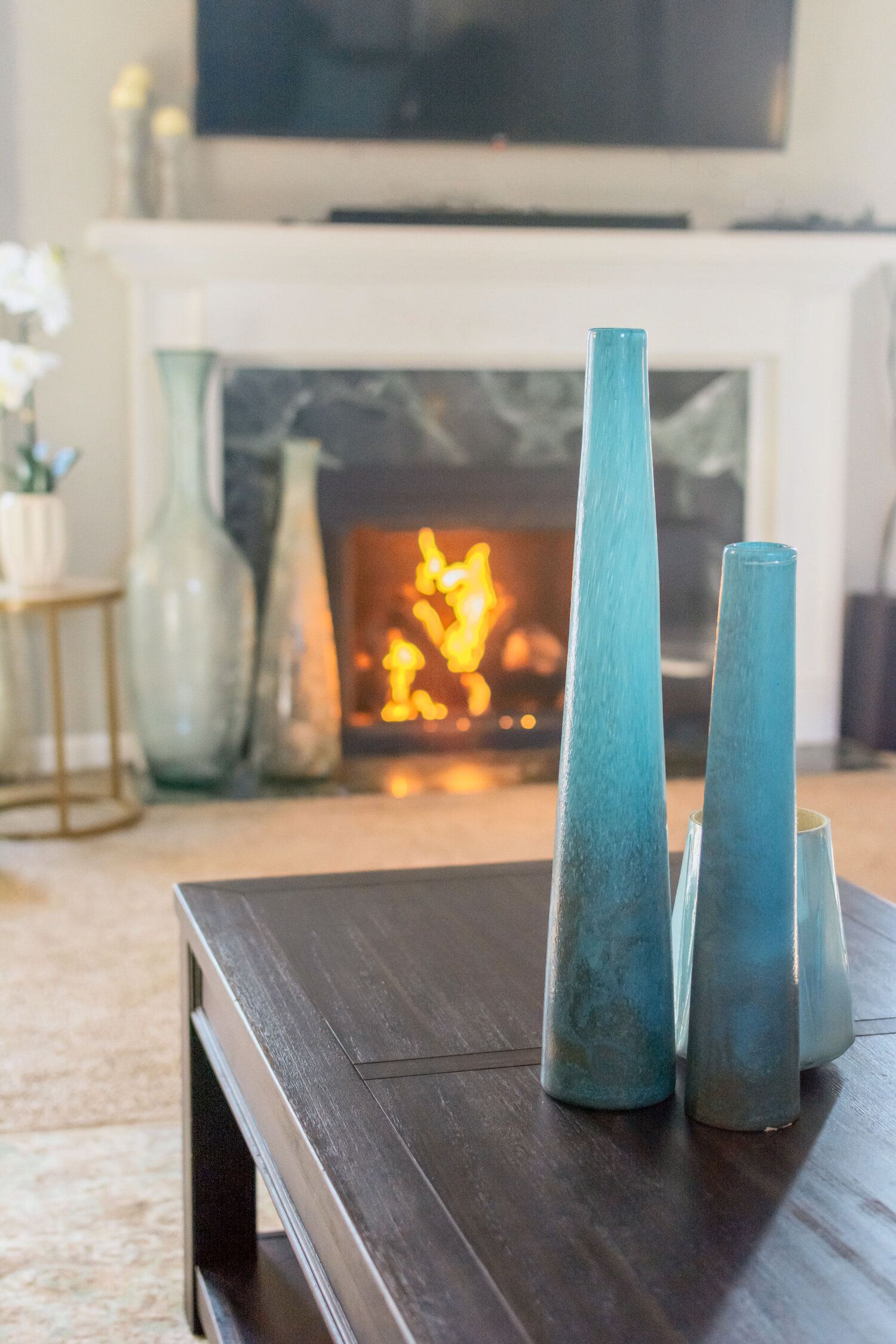 A living room with a fireplace and a coffee table with vases on it.