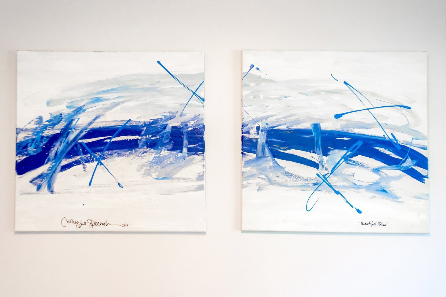 Two blue and white paintings are hanging on a white wall.