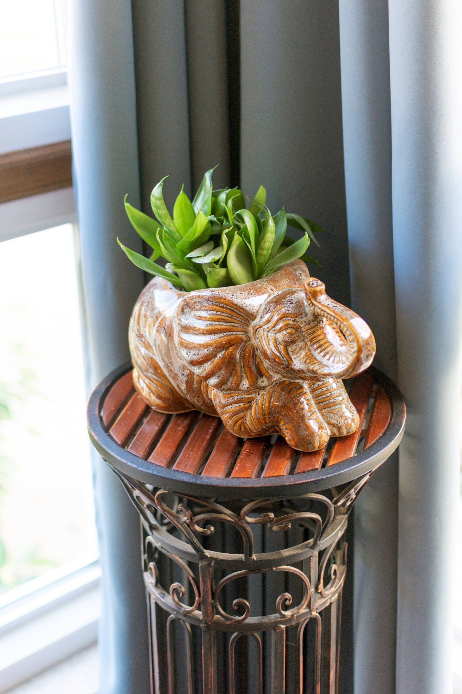 A statue of an elephant with a plant in it is sitting on a table next to a window.
