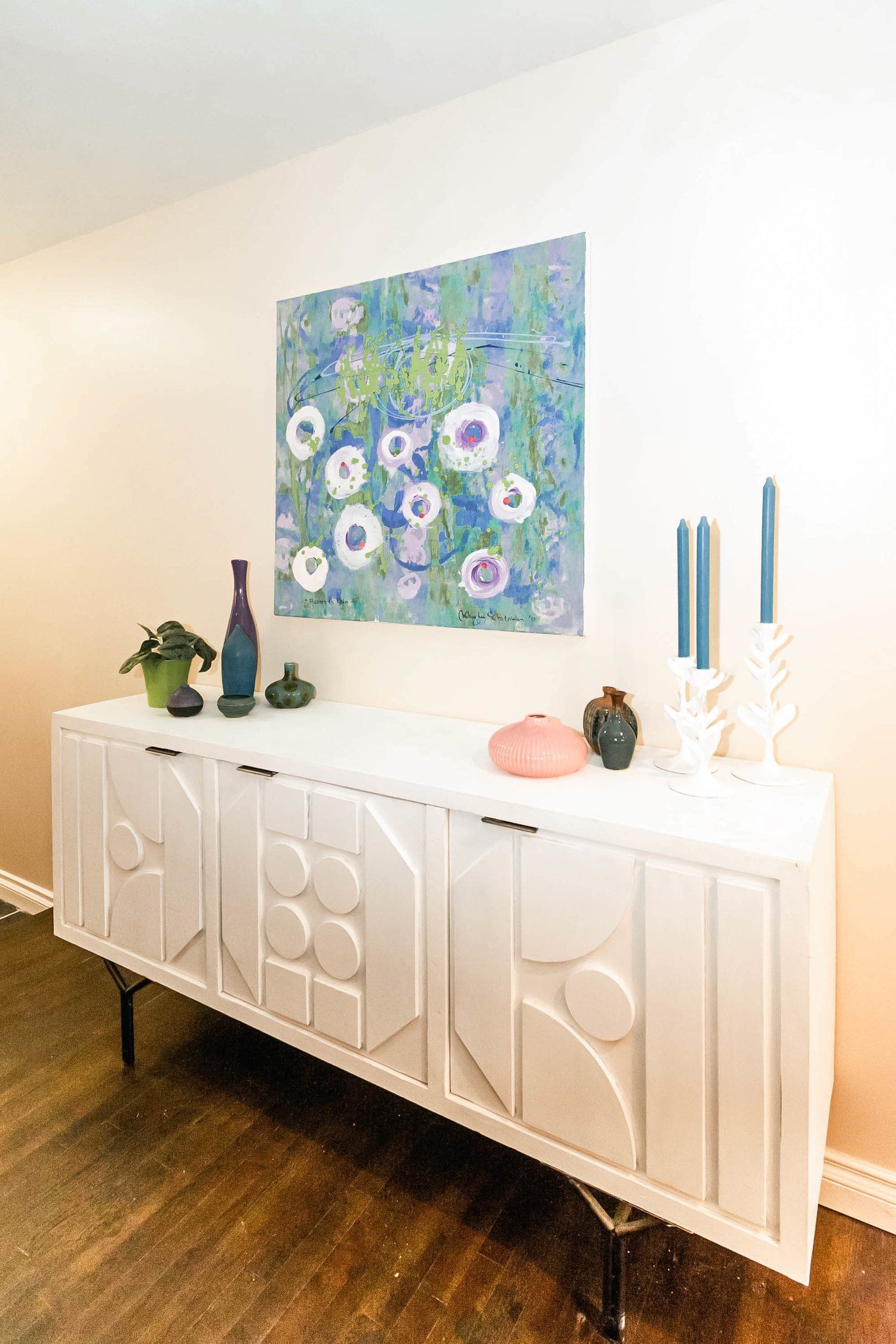 A white dresser with a painting on the wall above it.