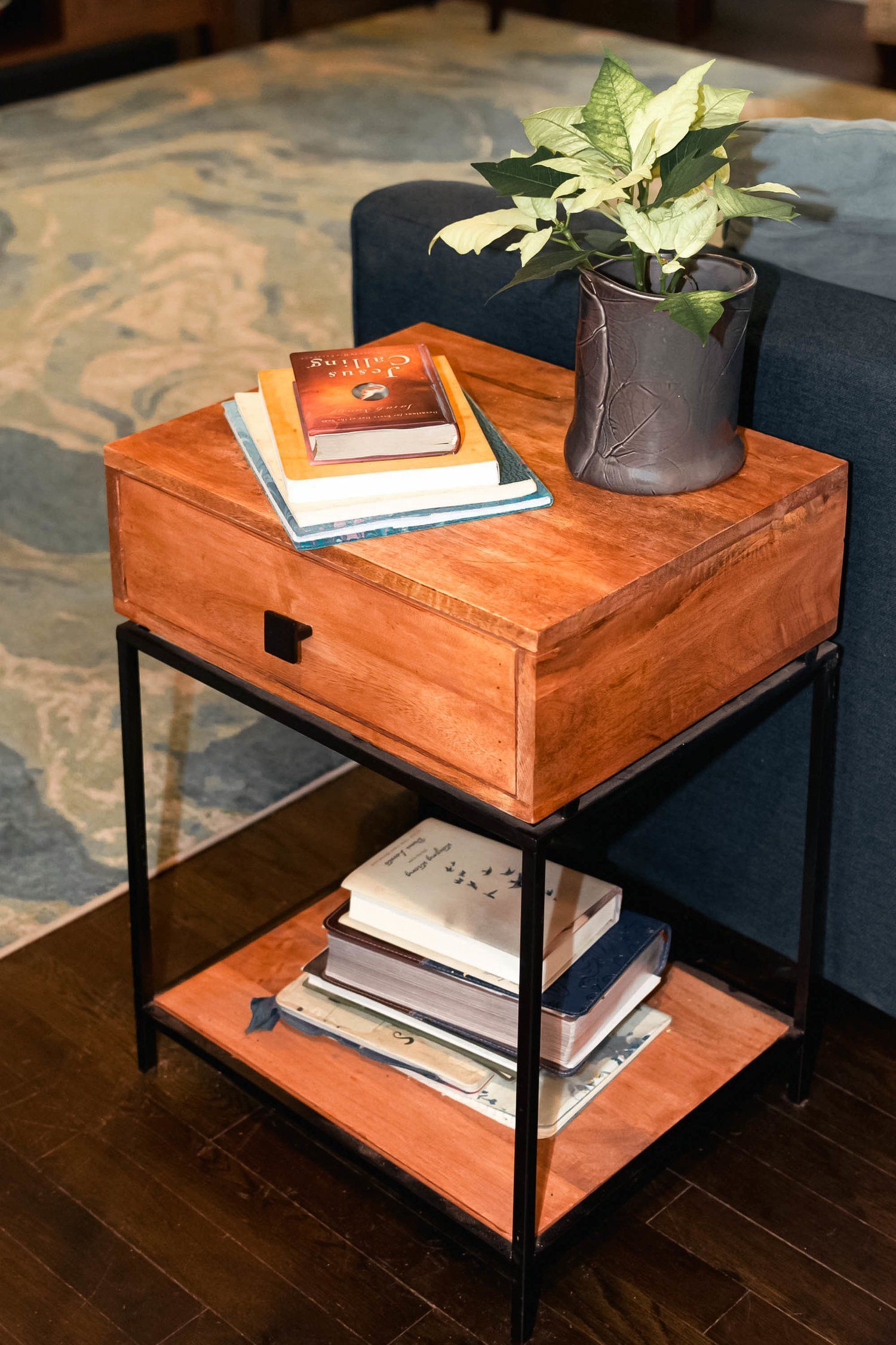 A wooden side table with books and a plant on it next to a couch.