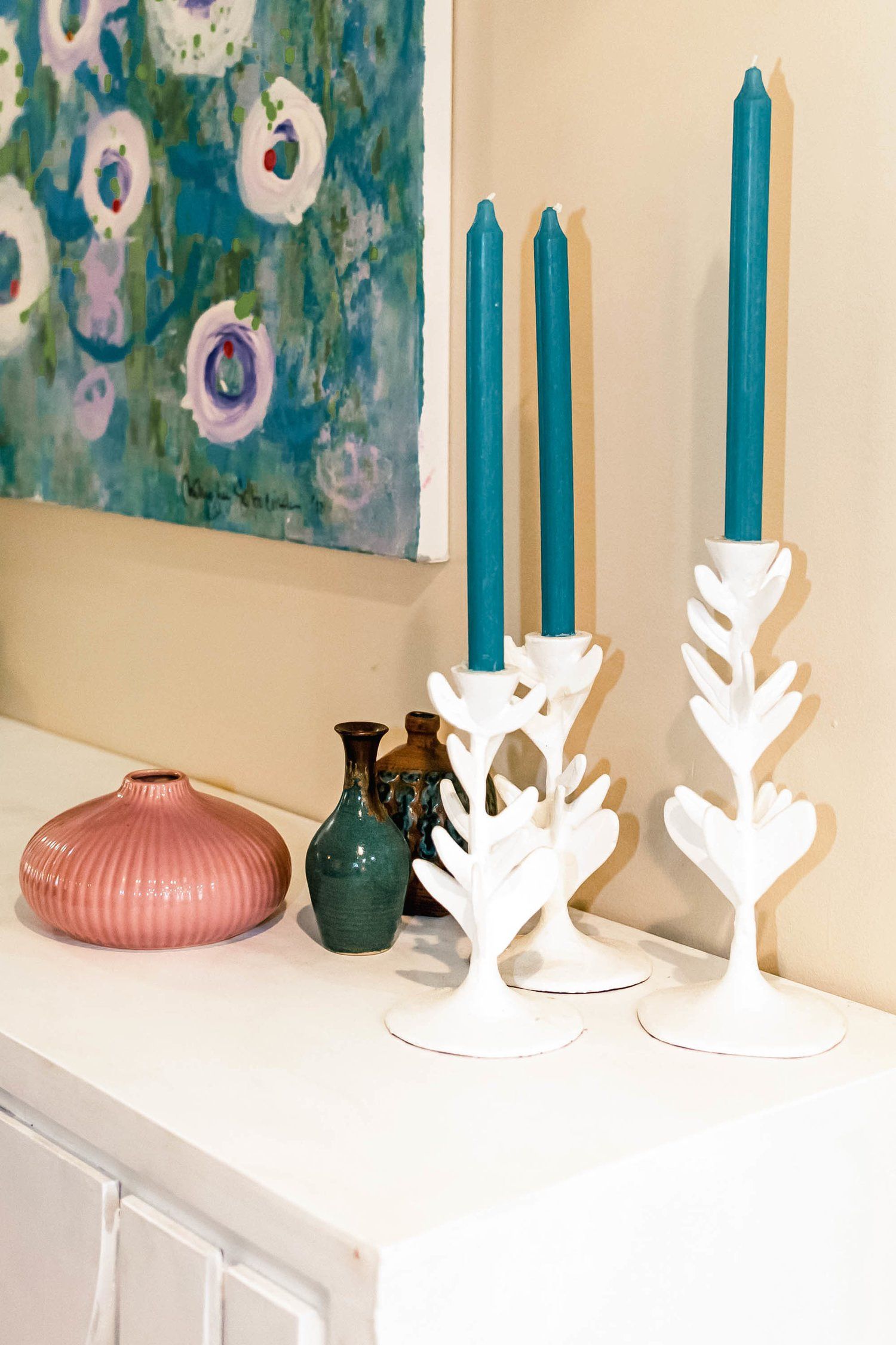 Three candles are sitting on a table next to vases and a painting.